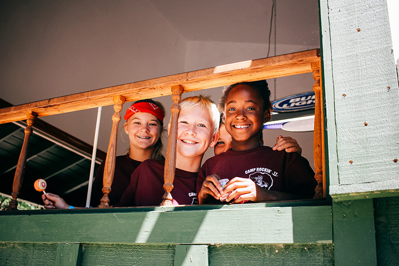 three campers smiling through a wood railing