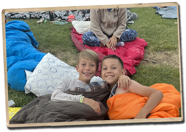 two campers next to each other in sleeping bags on the grass smiling for the camera