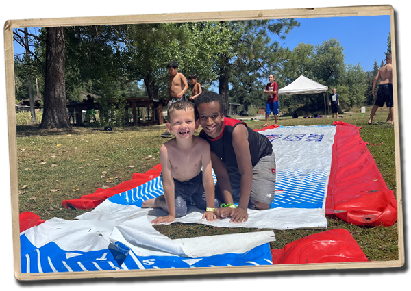two campers smiling for the camera on a slip and slide